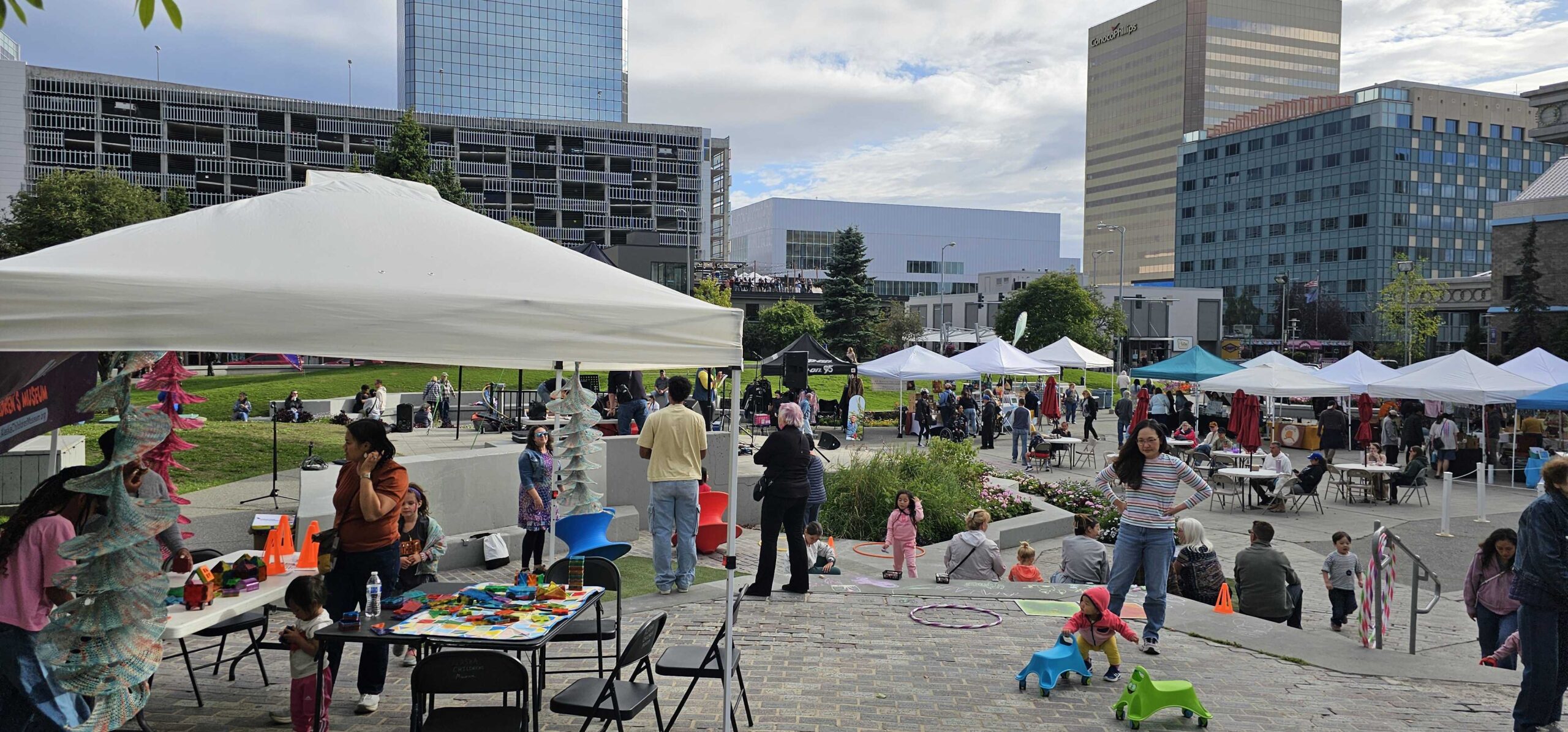 Summer night market: Children playing with children's museum toys and people moving between pop up tents in Town Square Park in Downtown Anchorage.